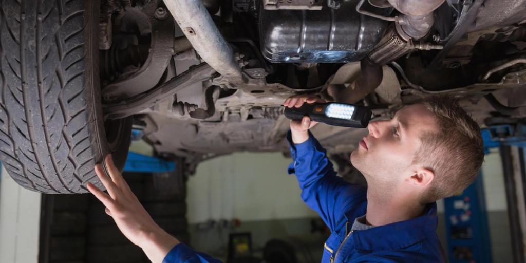 A mechanic looking at the underside of a car