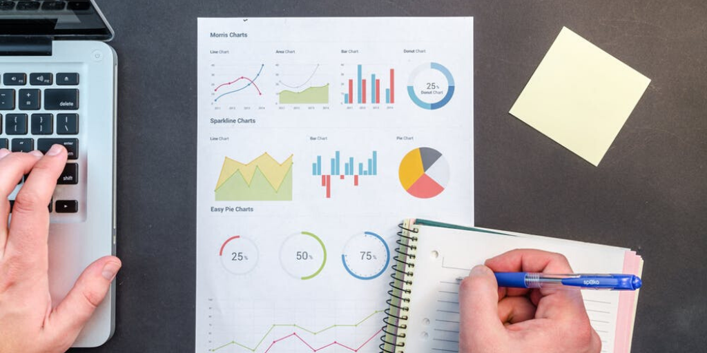 An office worker takes notes with a report of tables and charts on the desk