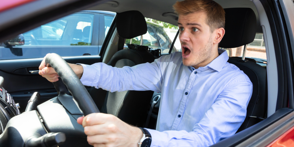 A shocked-looking man behind the wheel of a car