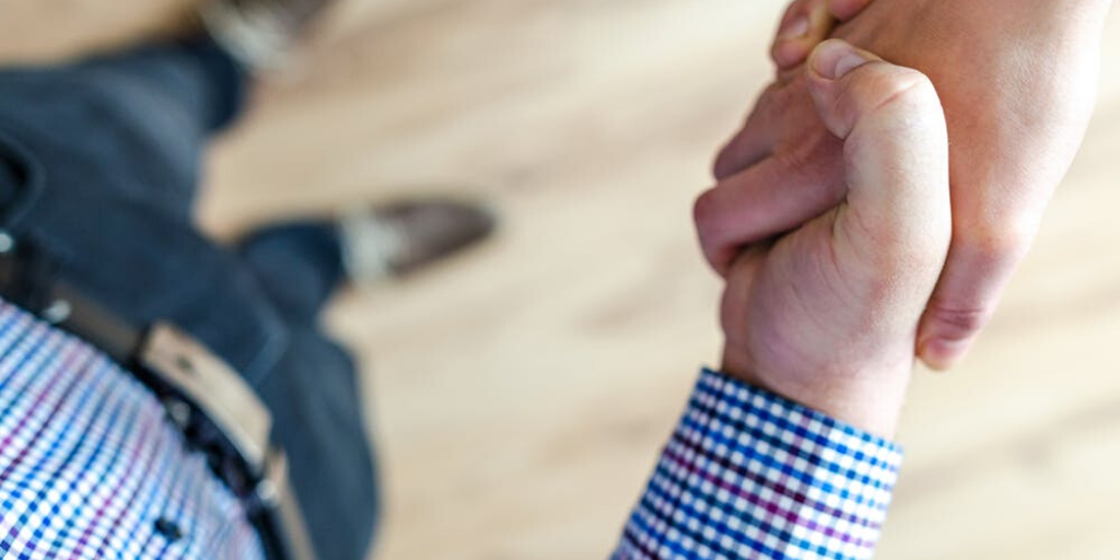 A man wearing a plaid shirt and jeans shakes hands with a companion