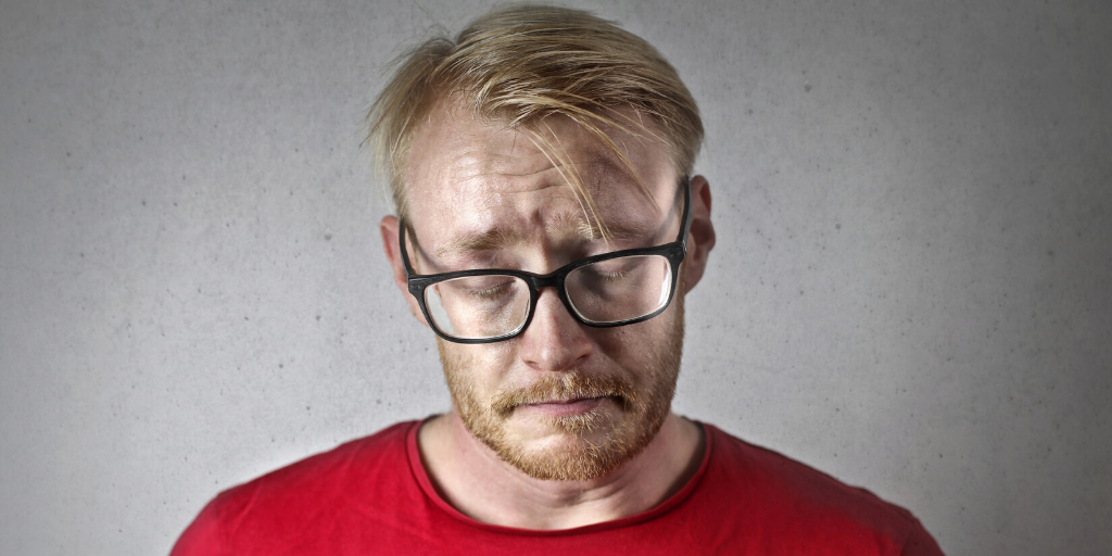A man in a red t-shirt appears sad or disappointed