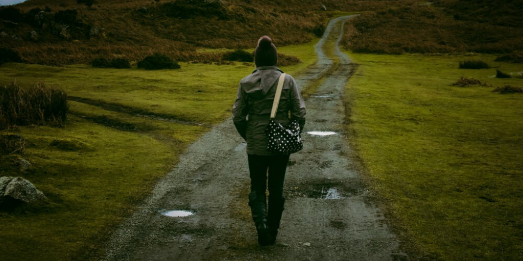 A woman walks alone down a long gravel path in the countryside