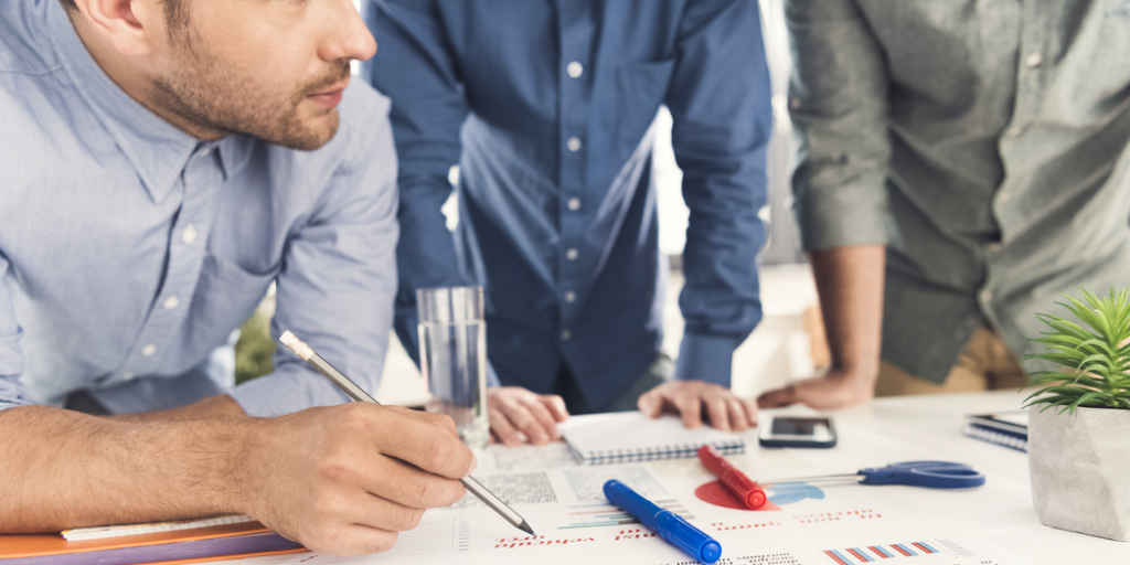 Three young businessmen leaning at a table and working at project together