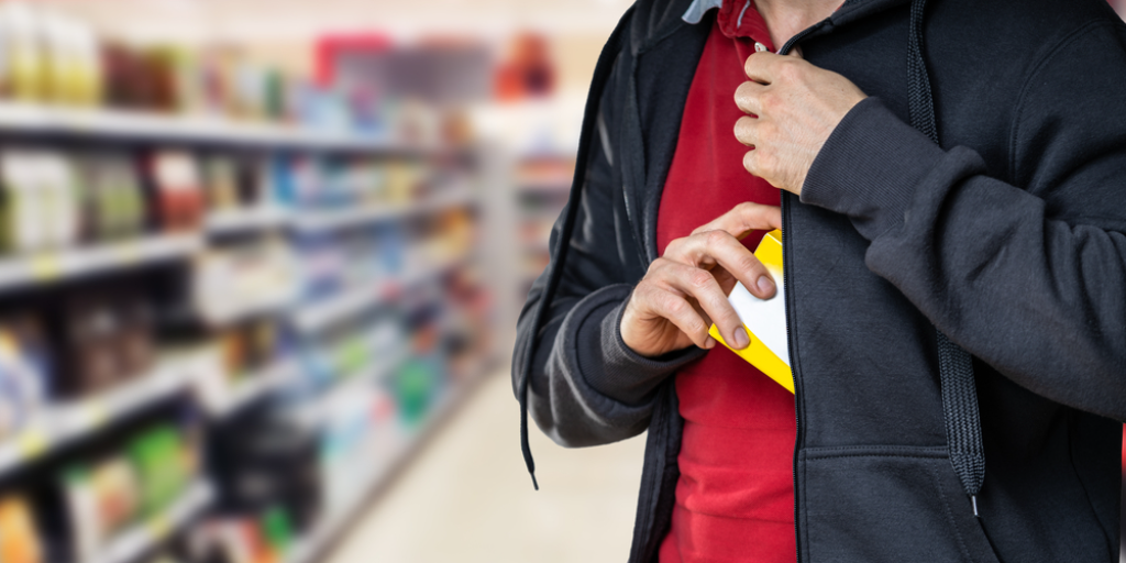 A man in a supermarket placing a yellow box inside his jacket.